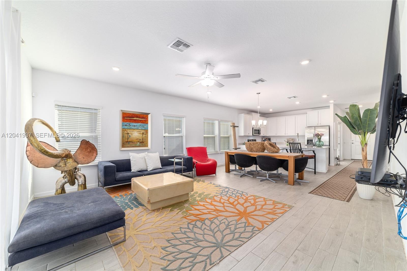 An open-concept living and dining area features white cabinetry, light wood-look flooring, and colorful decor — 7451 SW 76TH TER, Ocala FL 34481, OCALA, FL