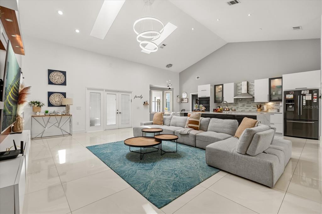 A bright, open-concept living room and kitchen featuring white tile floors and vaulted ceilings — 8050 RURAL RETREAT COURT, ORLANDO, FL