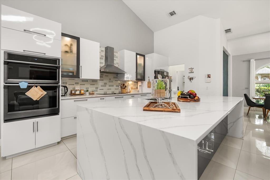 A modern kitchen features a large white marble waterfall island, white cabinetry, and stainless appliances — 8050 RURAL RETREAT COURT, ORLANDO, FL