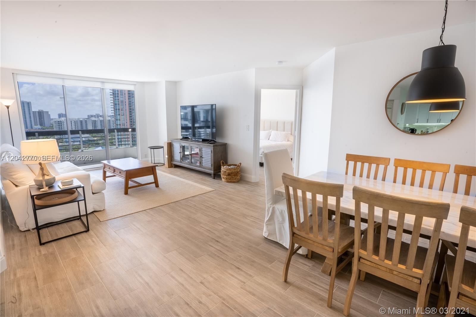 A bright living and dining area features light wood-look flooring and a balcony view — AVENTURA, FL