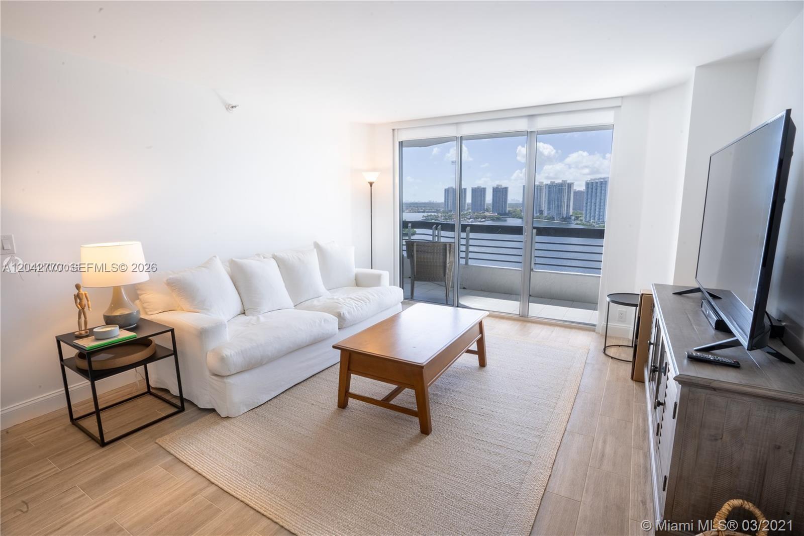 A living room features a white sofa, wooden coffee table, and a balcony with water views — AVENTURA, FL