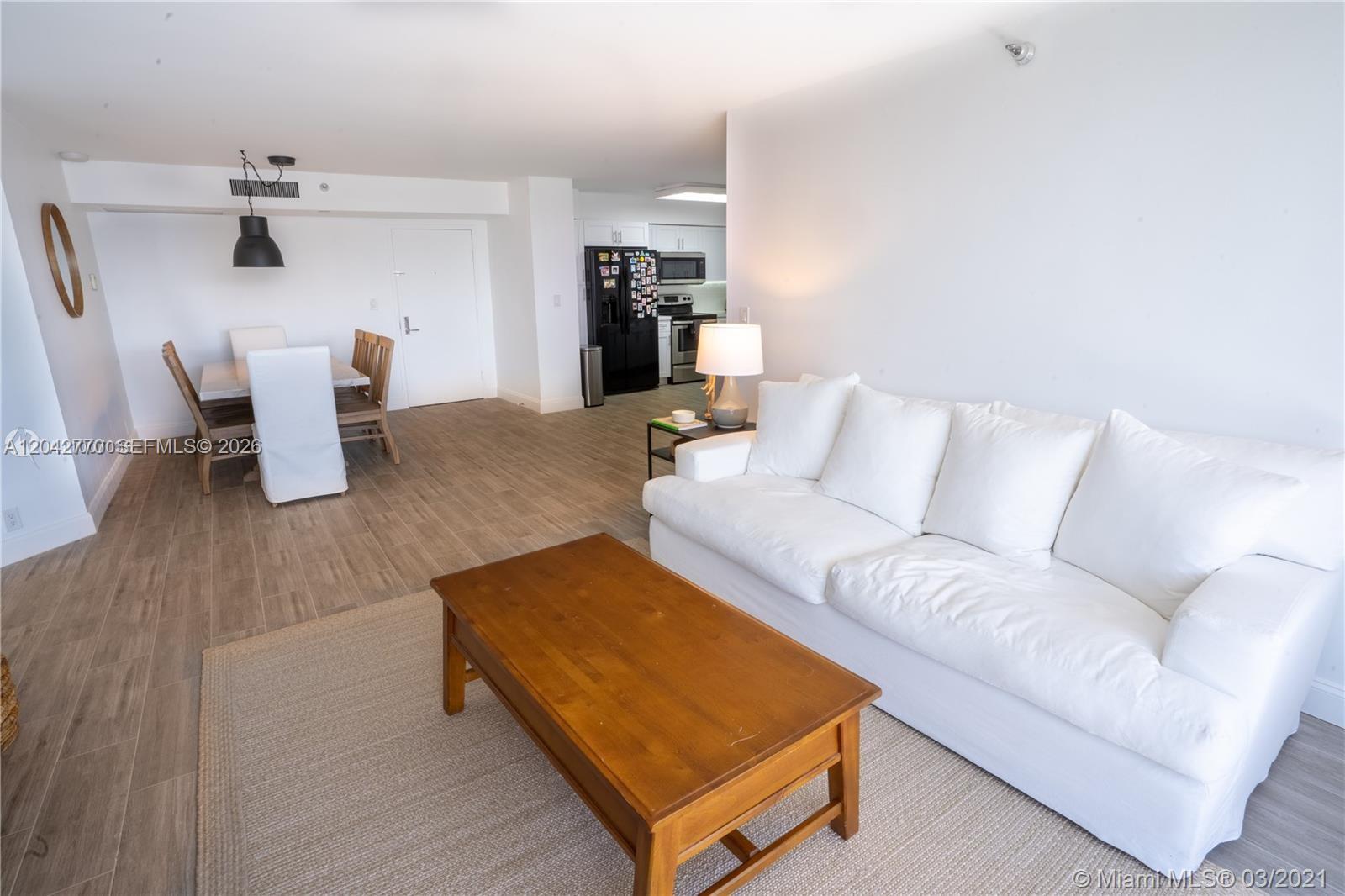 A living room with a white sofa and wooden coffee table opens to a dining area — AVENTURA, FL
