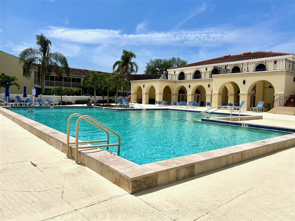 A large outdoor swimming pool sits in front of a multi-story building with arched walkways — 6101 34TH STREET W UNIT 22H, BRADENTON, FL