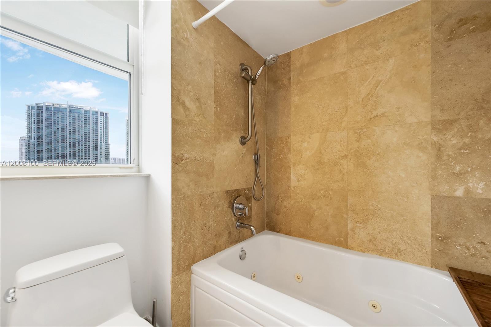 A bathroom features a jetted tub with tan tile walls and a view of buildings — 41 SE 5th St # 504, Miami FL 33131, MIAMI, FL