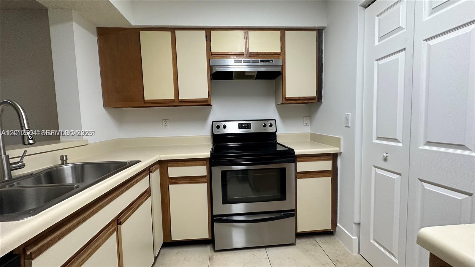 A kitchen features a stainless steel stove, beige countertops, and two-toned wood and cream cabinets — 1243 SW 46th Ave # 1111, Pompano Beach FL 33069, POMPANO BEACH, FL