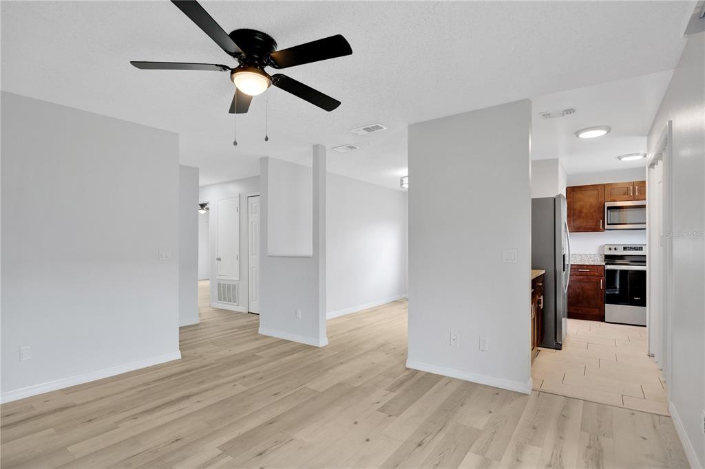 A living area with light wood-look flooring leads to an open kitchen with dark cabinets — 4100 PERSHING POINTE PLACE UNIT 3, ORLANDO, FL