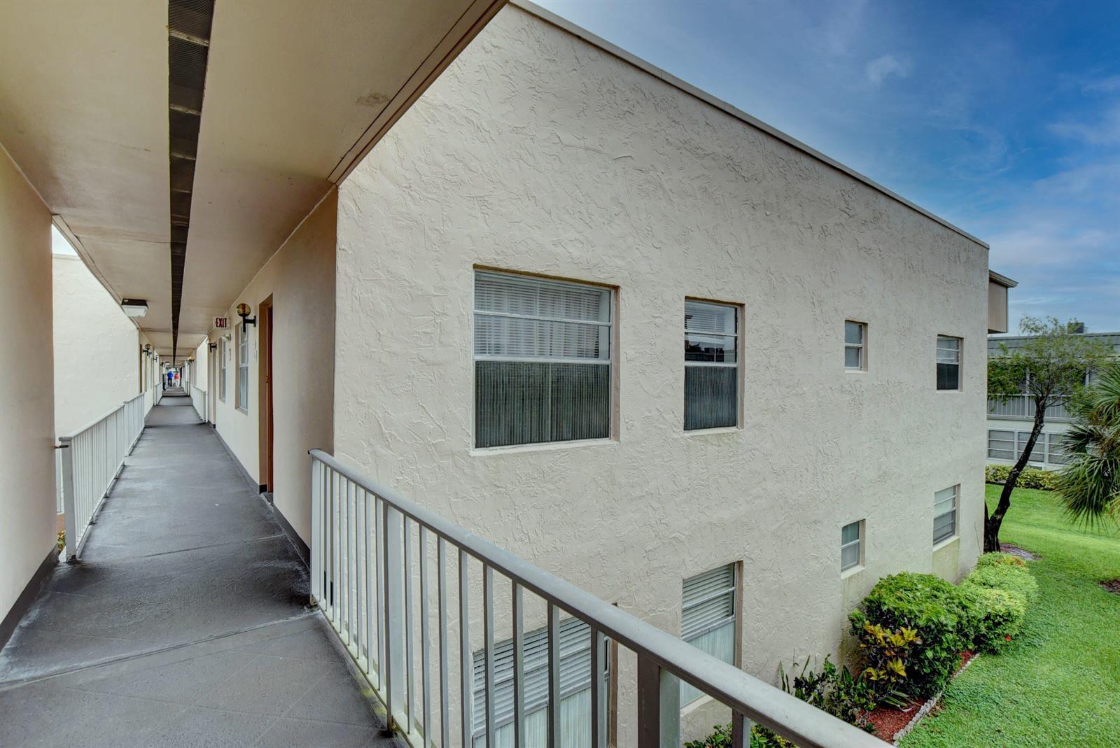 An exterior view of an apartment building with a concrete walkway and metal railings — 138 Flanders C, Delray Beach FL 33484, DELRAY BEACH, FL