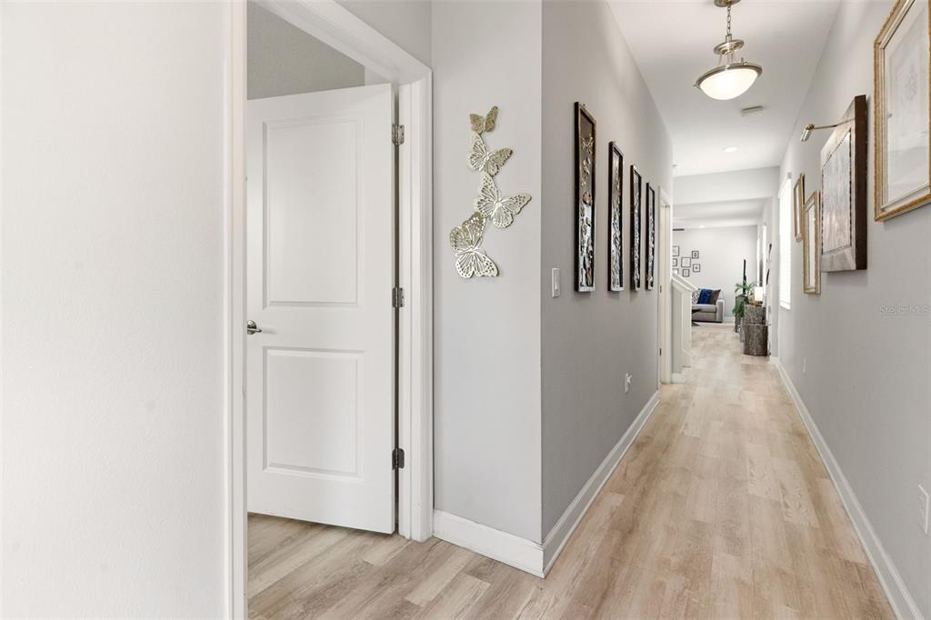 A hallway with light wood-look flooring features wall-mounted butterfly decor and framed artwork — 11932 HOMETOWN PLACE, ORLANDO, FL
