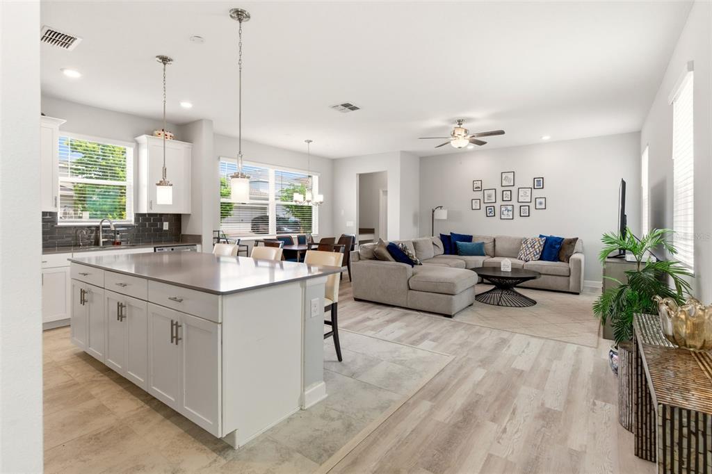 An open-concept kitchen with a large island overlooks a living room with a sectional sofa — 11932 HOMETOWN PLACE, ORLANDO, FL