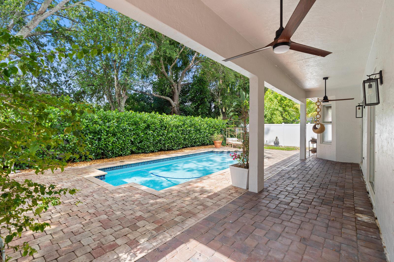 A covered brick patio overlooks a rectangular swimming pool bordered by a tall green hedge — 19360 SW 29th Court, Miramar FL 33029, MIRAMAR, FL
