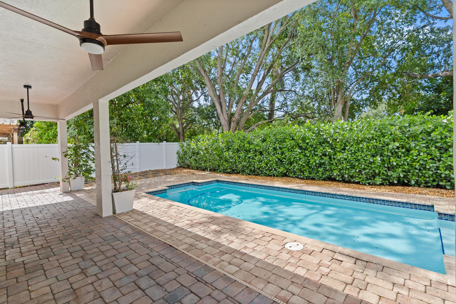 A covered patio with brick pavers overlooks a rectangular swimming pool and a privacy hedge — 19360 SW 29th Court, Miramar FL 33029, MIRAMAR, FL
