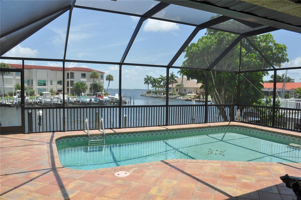 A screened-in pool patio overlooks a canal with boats and residential buildings in the distance — 2750 AQUA COURT, PUNTA GORDA, FL