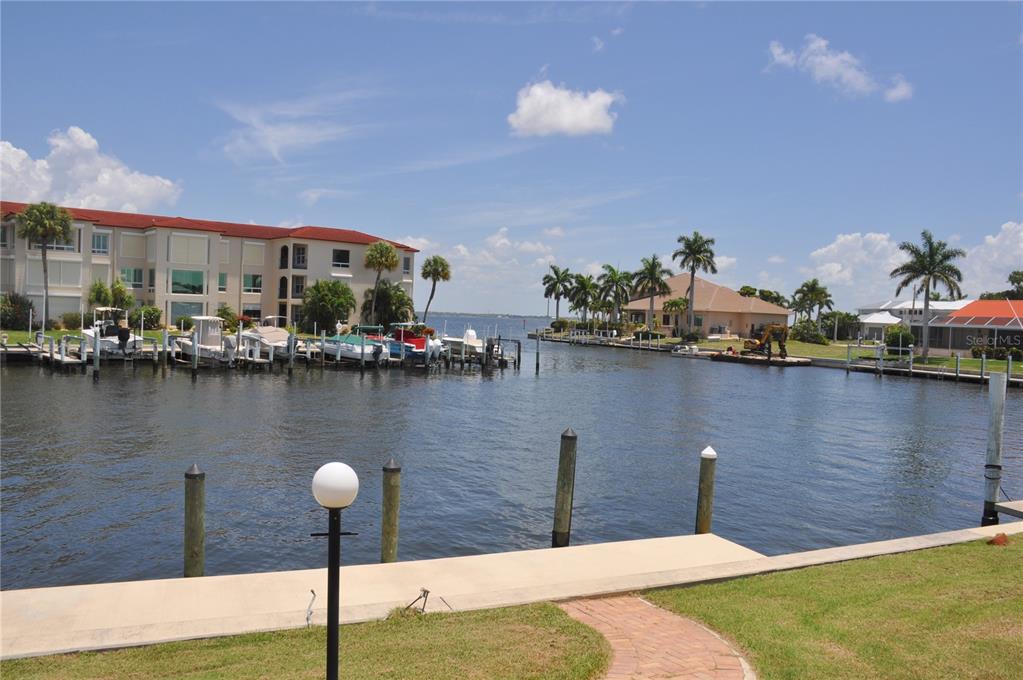 A canal view features a multi-story building, docked boats, palm trees, and a concrete bulkhead — 2750 AQUA COURT, PUNTA GORDA, FL
