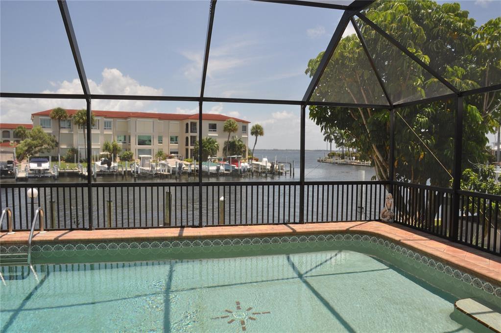 A swimming pool with a compass inlay sits inside a screened enclosure overlooking a canal — 2750 AQUA COURT, PUNTA GORDA, FL