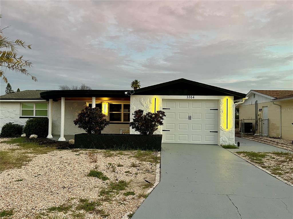 A single-story house with a white textured facade, black trim, and a gray concrete driveway — 3314 TRASK DRIVE, HOLIDAY, FL