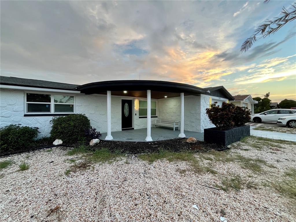 A white house with a curved porch roof, three columns, and a gravel front yard — 3314 TRASK DRIVE, HOLIDAY, FL
