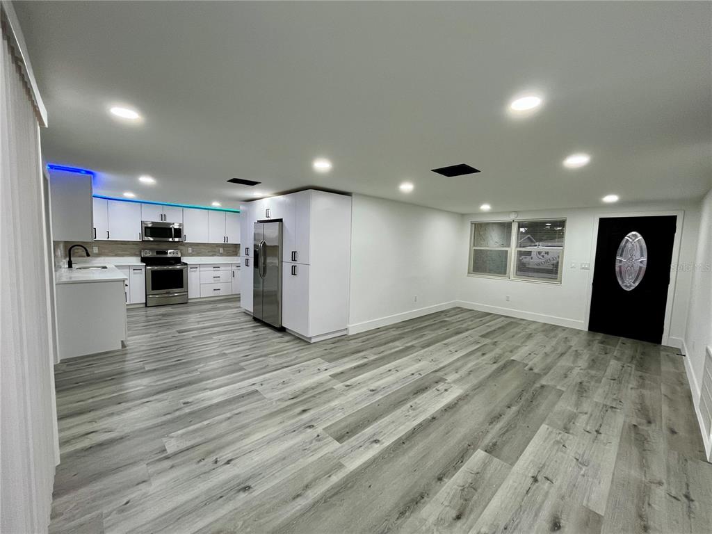 A modern, open-concept kitchen and living area featuring white cabinets, stainless appliances, and wood-look flooring — 3314 TRASK DRIVE, HOLIDAY, FL