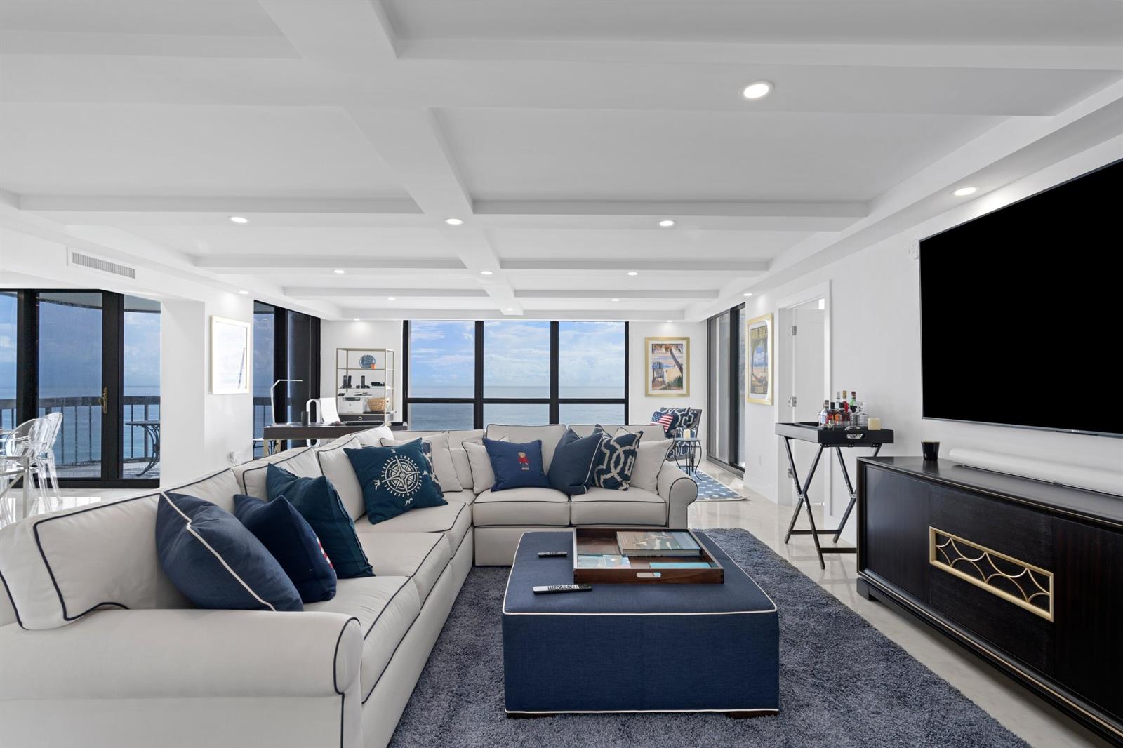 A living room features a large sectional sofa, a blue ottoman, and floor-to-ceiling ocean views — 5380 N Ocean Drive # 10d, Riviera Beach FL 33404, RIVIERA BEACH, FL