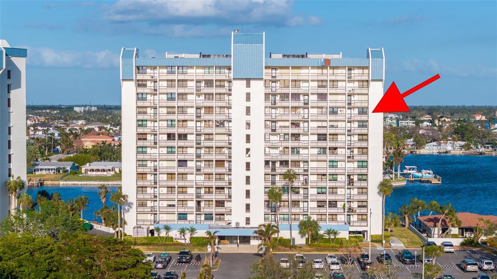 An exterior view of a multi-story apartment building with a red arrow pointing to a balcony — 9415 BLIND PASS ROAD UNIT 1006, ST PETE BEACH, FL
