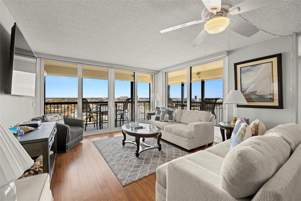 A living room features light-colored sofas, a coffee table, wood flooring, and a balcony view — 9415 BLIND PASS ROAD UNIT 1006, ST PETE BEACH, FL