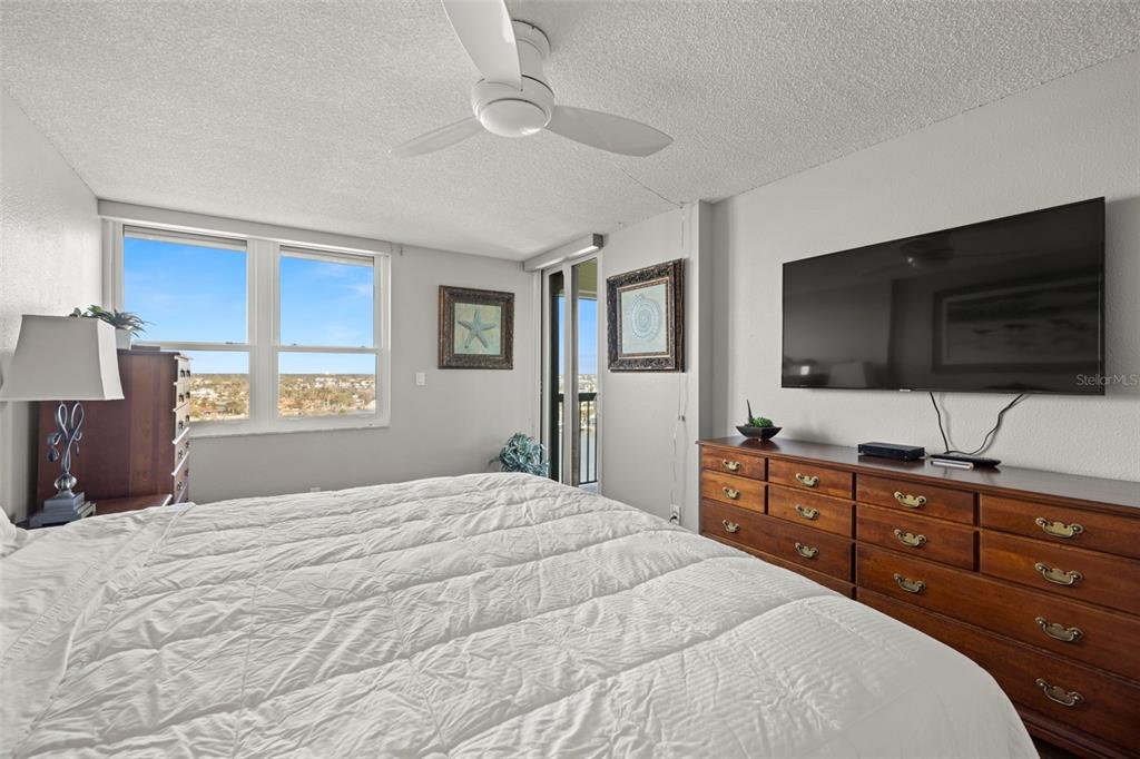 A bedroom features a bed, a wooden dresser with a television, and a ceiling fan — 9415 BLIND PASS ROAD UNIT 1006, ST PETE BEACH, FL