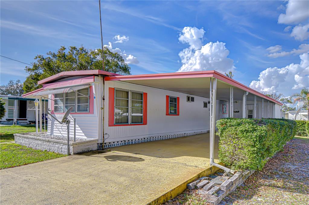 A white mobile home with a pink-trimmed roof and a covered carport on a sunny day — 37427 HAMMOND DRIVE, ZEPHYRHILLS, FL
