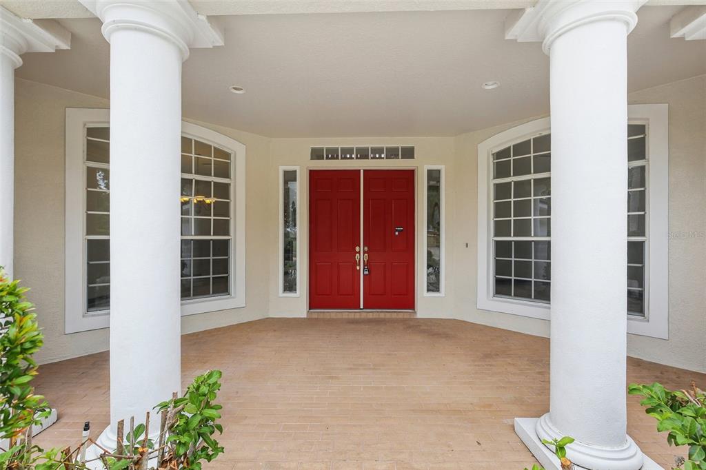 A covered entryway features two white columns, a brick floor, and bright red double doors — 3062 SUTTON WOODS DRIVE, PLANT CITY, FL