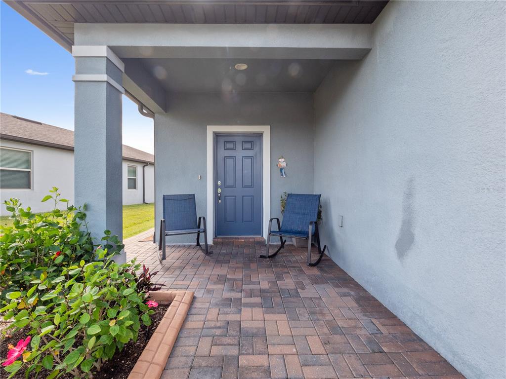 A covered front porch features a blue door, two rocking chairs, and brick pavers — 3570 SOUTHERN CROSS LOOP, KISSIMMEE, FL