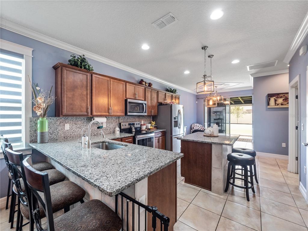 A kitchen features wood cabinets, granite countertops, a center island, and tile flooring — 3570 SOUTHERN CROSS LOOP, KISSIMMEE, FL