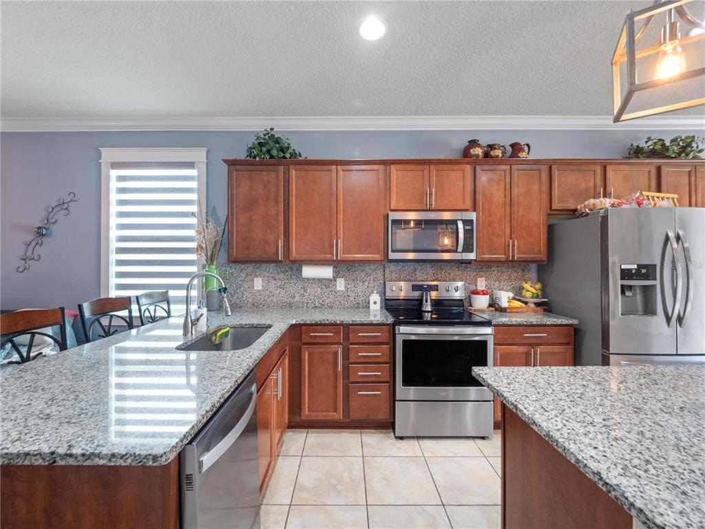 A kitchen features wood cabinets, granite countertops, stainless steel appliances, and a large island — 3570 SOUTHERN CROSS LOOP, KISSIMMEE, FL