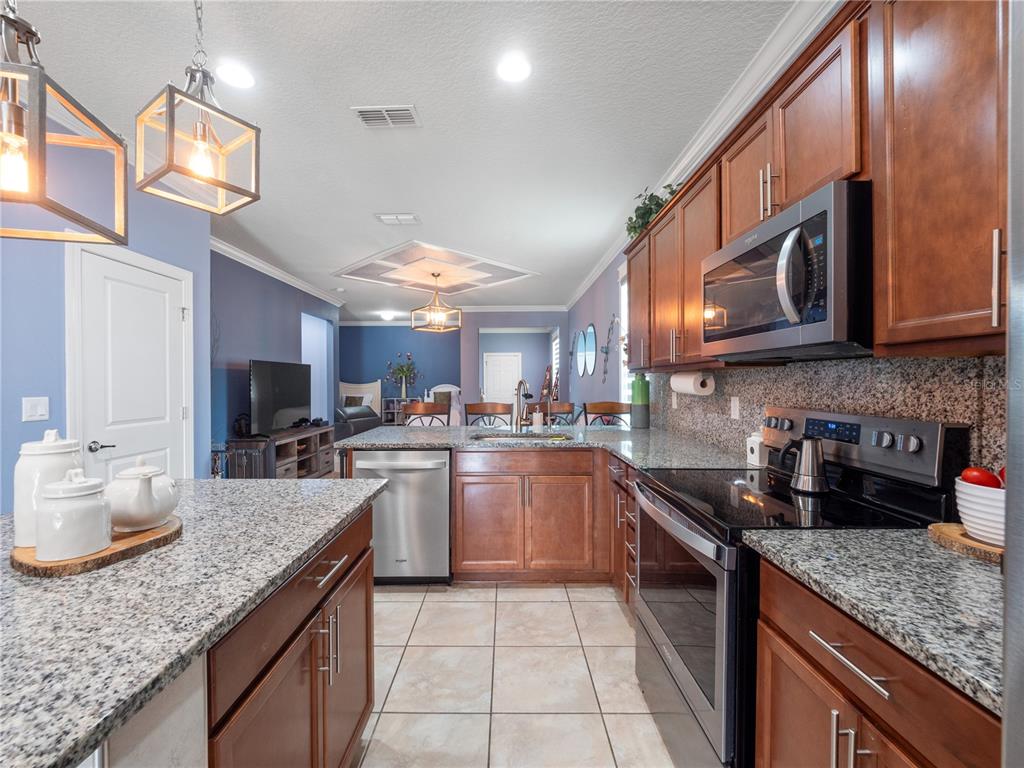 A kitchen with granite countertops, stainless steel appliances, and wood cabinets opens to a living area — 3570 SOUTHERN CROSS LOOP, KISSIMMEE, FL