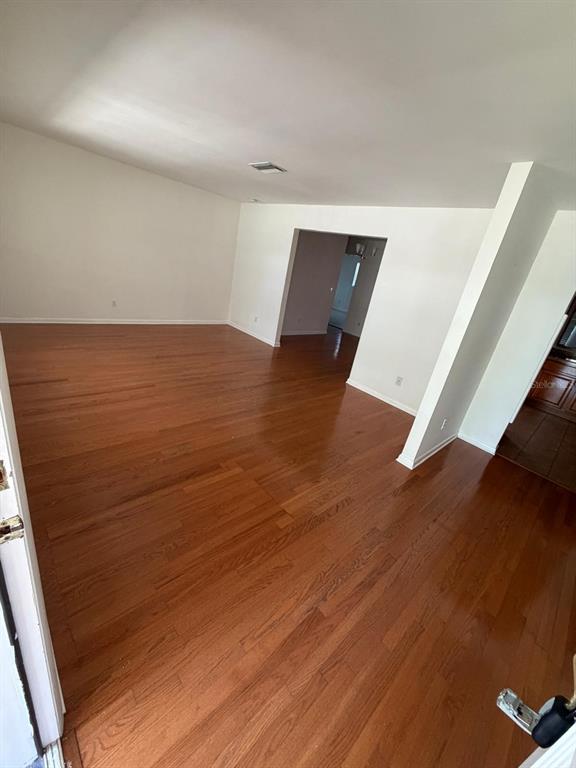 An empty room with hardwood flooring and white walls leads to an adjacent hallway — 11102 28TH STREET, TAMPA, FL