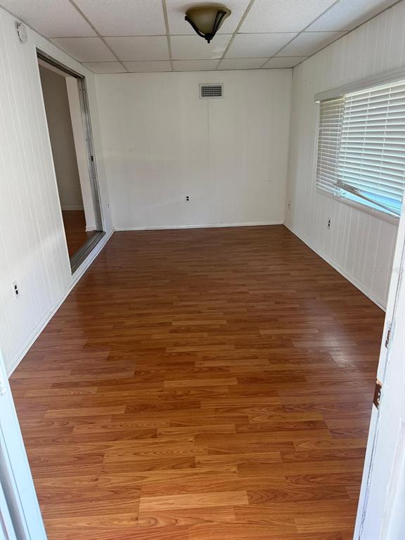 An empty room with wood-look laminate flooring, white paneled walls, and a window with blinds — 11102 28TH STREET, TAMPA, FL