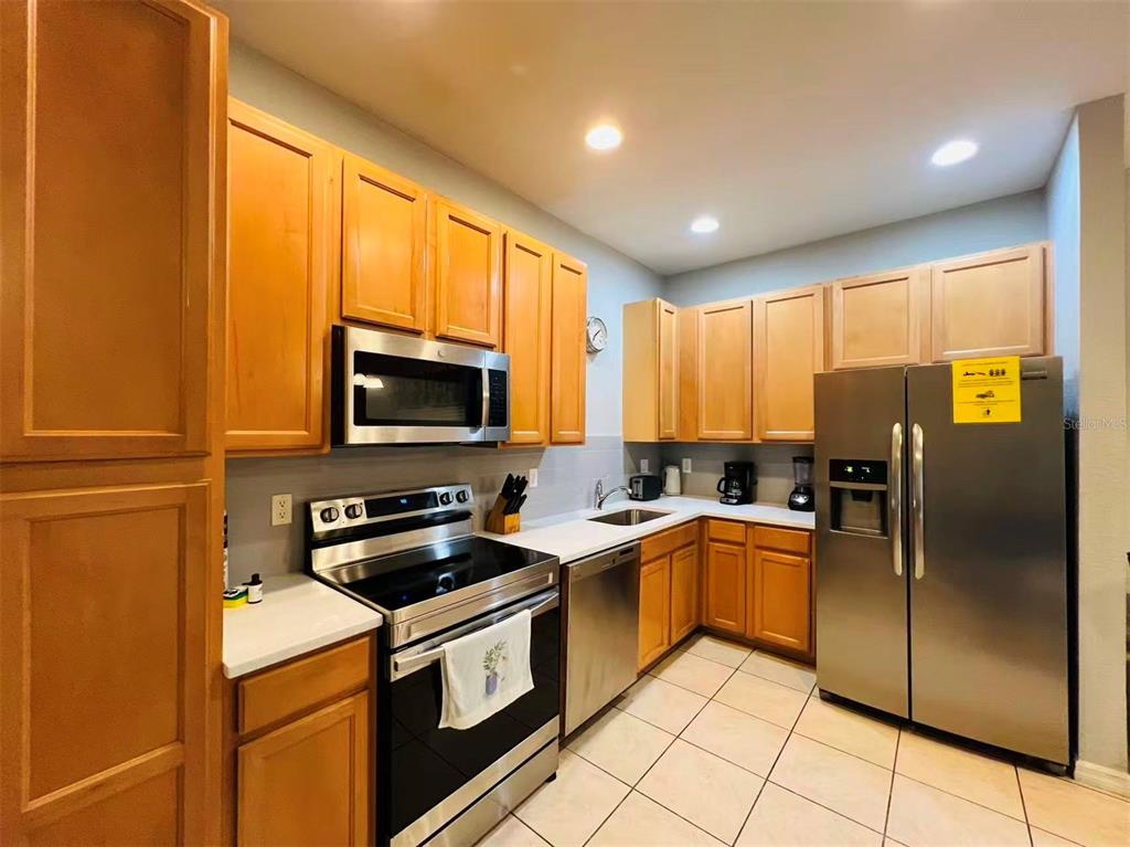 A kitchen features light wood cabinets, stainless steel appliances, and beige tile flooring — 2356 CARAVELLE CIRCLE, KISSIMMEE, FL