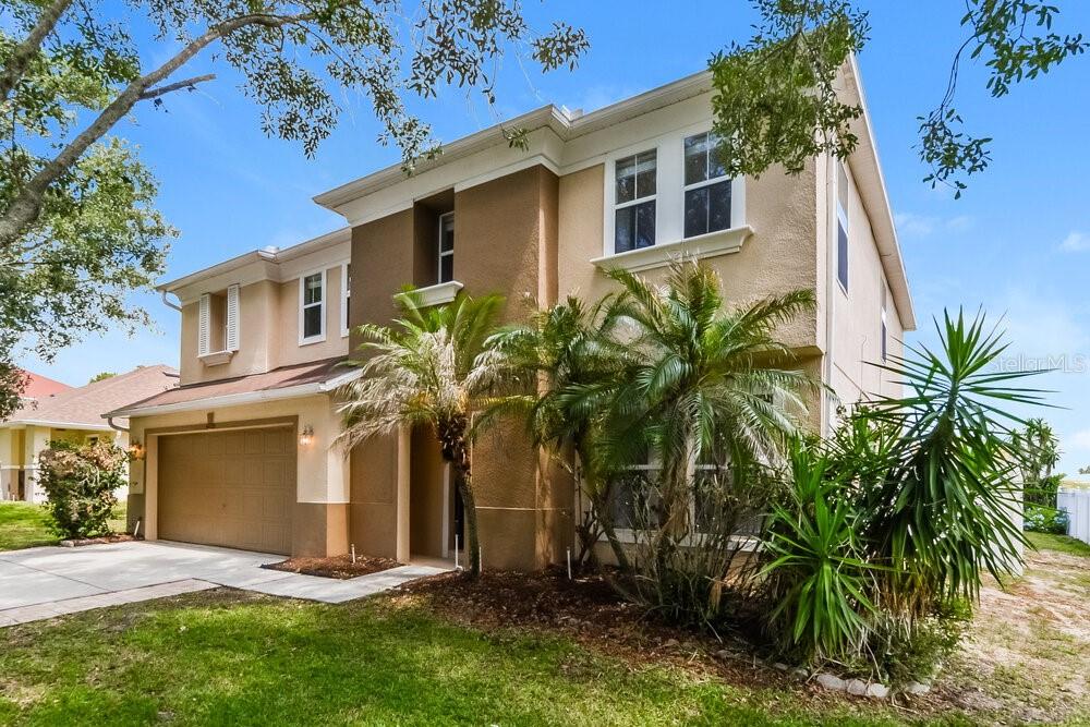 A two-story suburban house with a tan stucco exterior, a two-car garage, and palm trees — 4729 BARBADOS LOOP, CLERMONT, FL