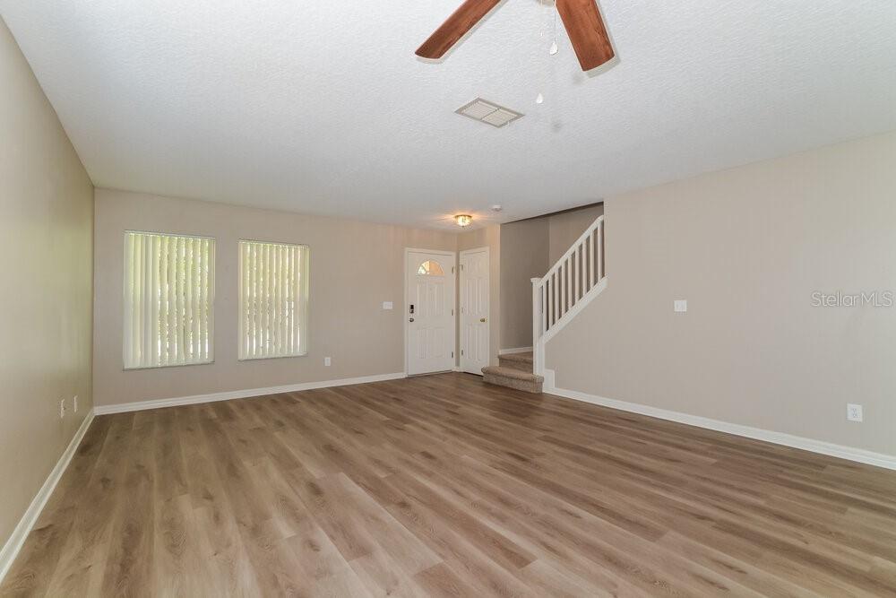 A living room features wood-look flooring, a ceiling fan, and stairs leading to an upper level — 4729 BARBADOS LOOP, CLERMONT, FL