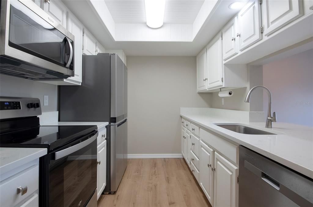 A galley kitchen features white cabinets, stainless steel appliances, light countertops, and wood-look flooring — 2593 COUNTRYSIDE BOULEVARD UNIT 7210, CLEARWATER, FL
