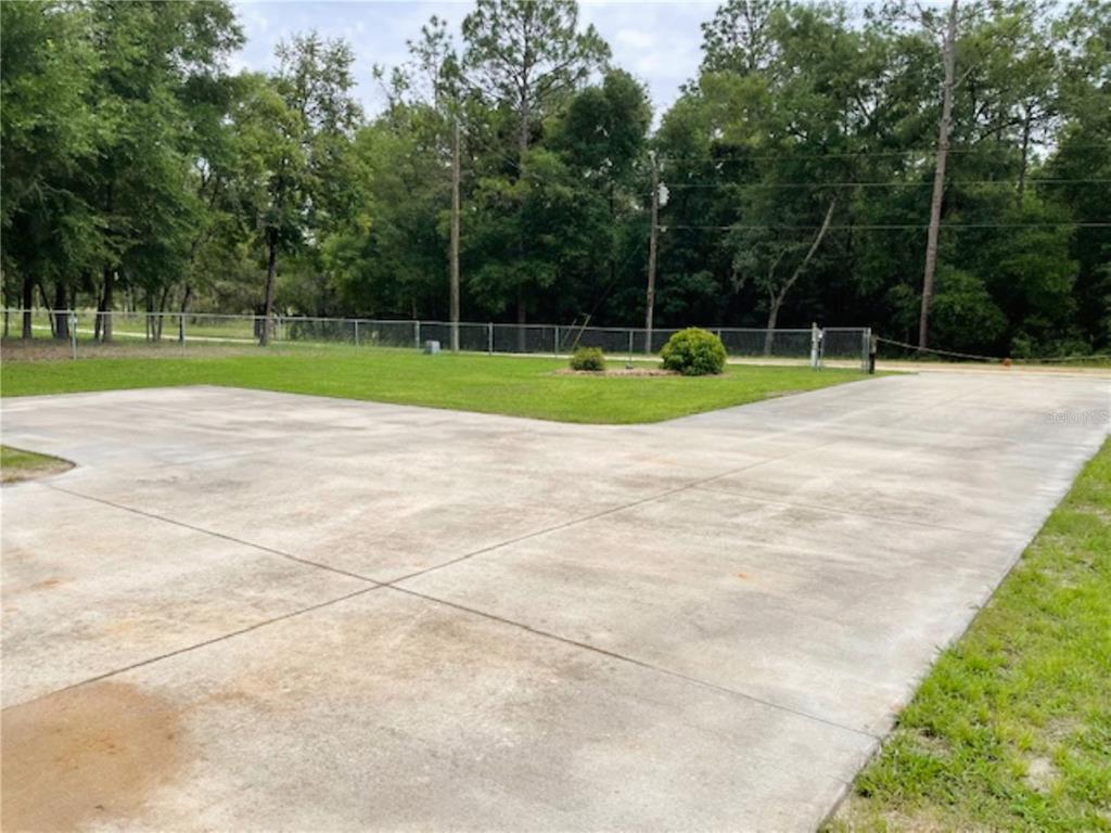 A large concrete driveway leads to a fenced grassy yard with trees in the background — 11931 SW 41ST PLACE, OCALA, FL