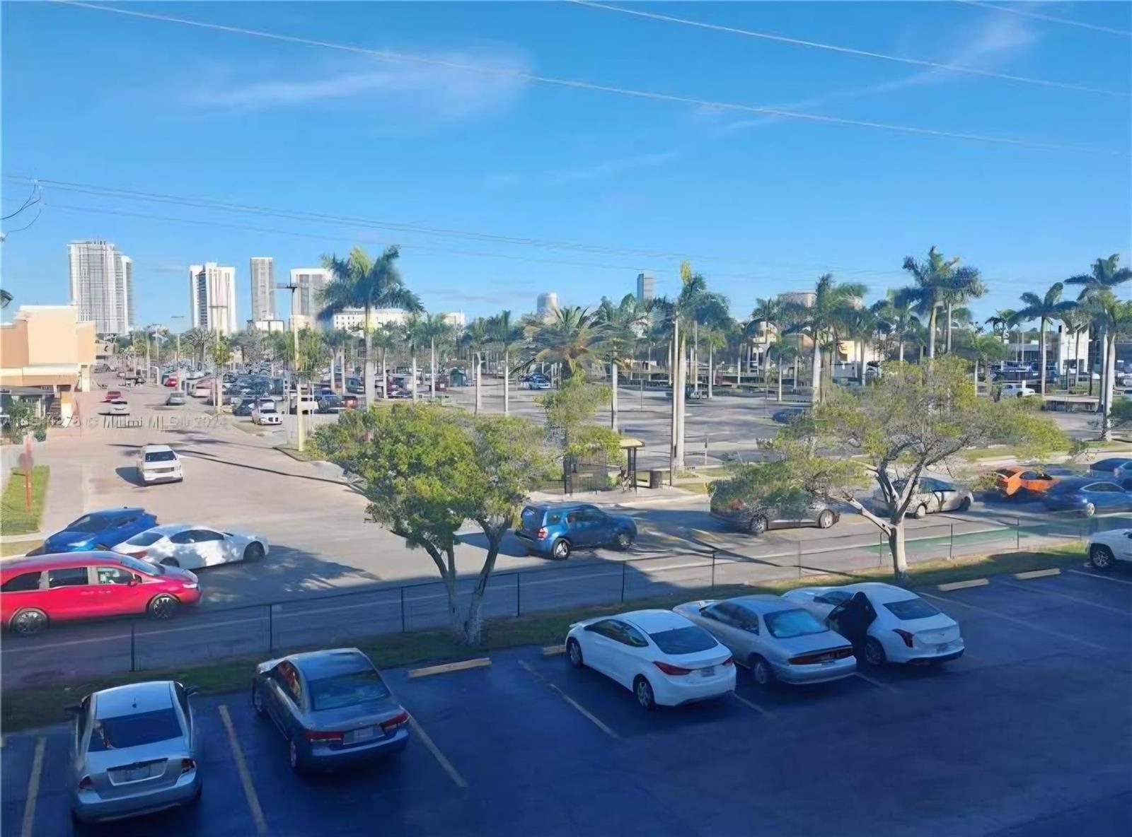 An elevated view shows a parking lot with several cars and palm trees under blue skies — 1333 E Hallandale Beach Boulevard # 305, Hallandale Beach FL 33009, HALLANDALE BEACH, FL