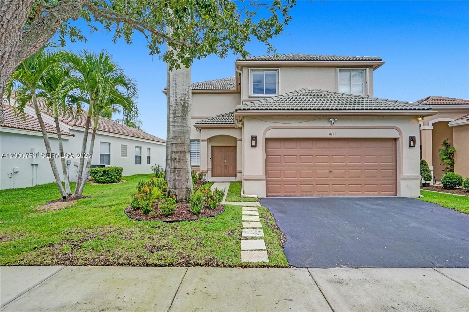 A two-story suburban house features a tan stucco exterior, a tile roof, and a driveway — 1871 Silverbell Ter, Weston FL 33327, WESTON, FL