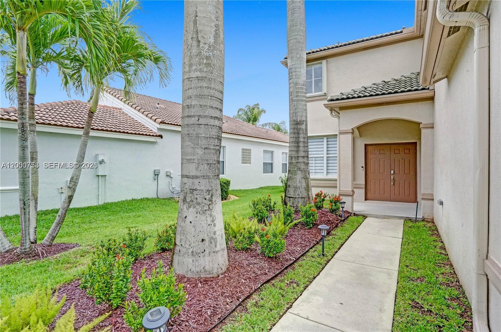 A concrete walkway leads to the front entrance of a two-story house with palm trees — 1871 Silverbell Ter, Weston FL 33327, WESTON, FL