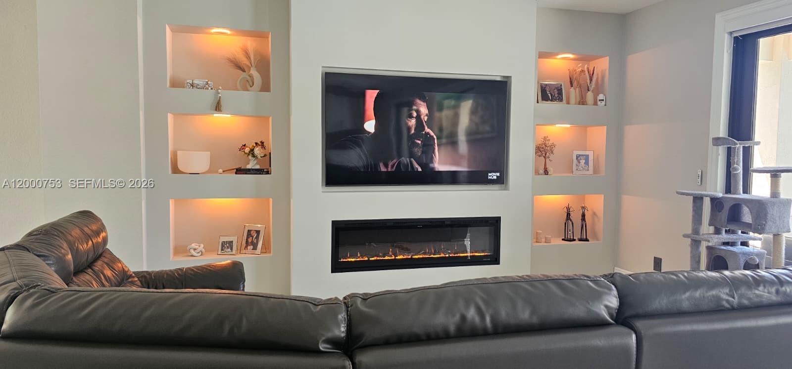 A living room features a wall-mounted television above a linear fireplace with built-in illuminated shelving — 1871 Silverbell Ter, Weston FL 33327, WESTON, FL