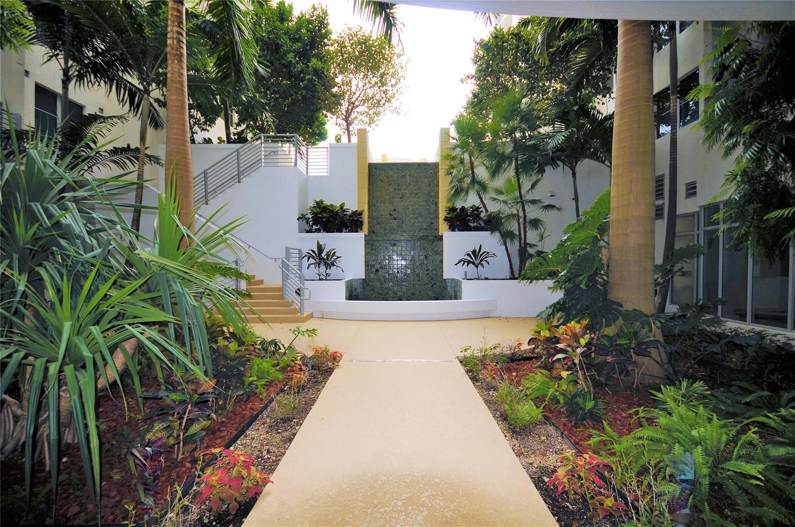 A paved walkway leads toward a tiered water feature surrounded by tropical landscaping and stairs — 1830 Radius Drive # 707, Hollywood FL 33020, HOLLYWOOD, FL
