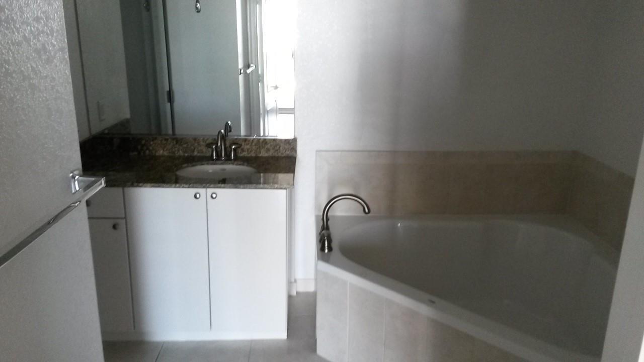 A bathroom features a white vanity with a granite countertop and a corner soaking tub — 1830 Radius Drive # 707, Hollywood FL 33020, HOLLYWOOD, FL