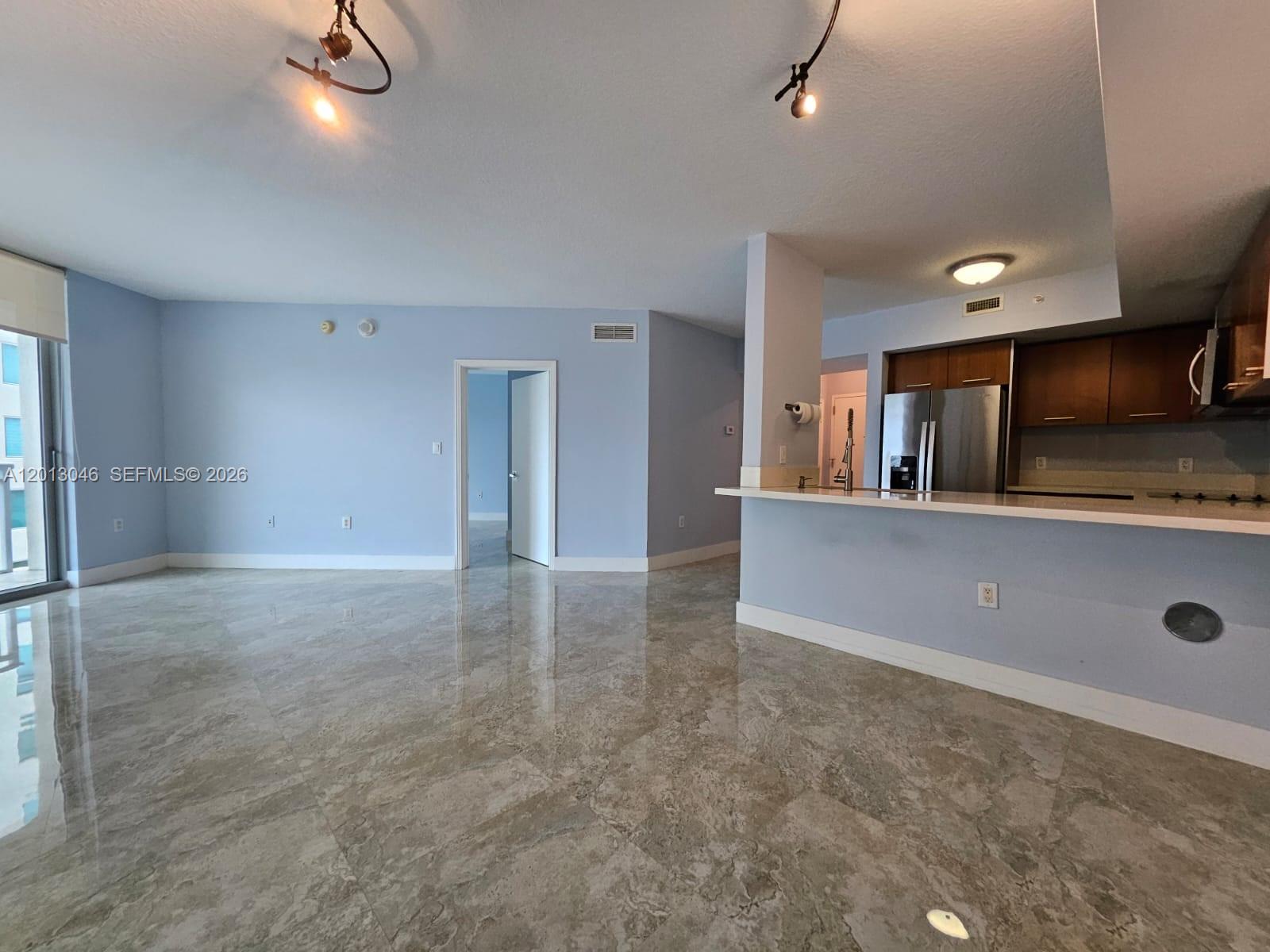 An open-concept living area features light blue walls, polished tile flooring, and a kitchen peninsula — 9055 SW 73rd Ct # 1008, Miami FL 33156, MIAMI, FL