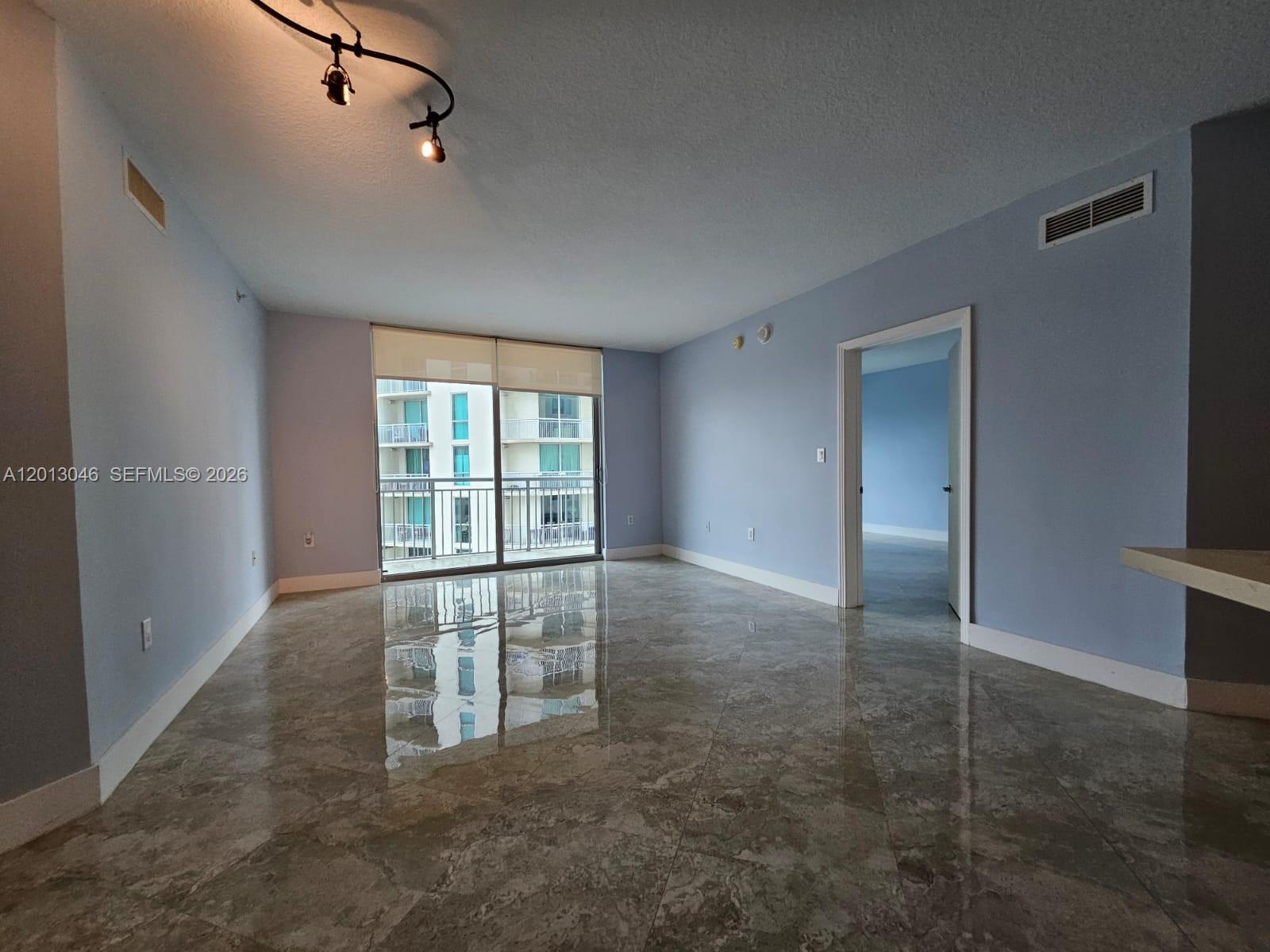 An empty living room features light blue walls, polished marble floors, and a balcony view — 9055 SW 73rd Ct # 1008, Miami FL 33156, MIAMI, FL