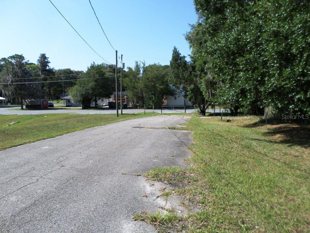 An asphalt driveway leads toward a road with trees and houses in the background — 000 BLUE HERON CT UNIT 000, DUNNELLON, FL