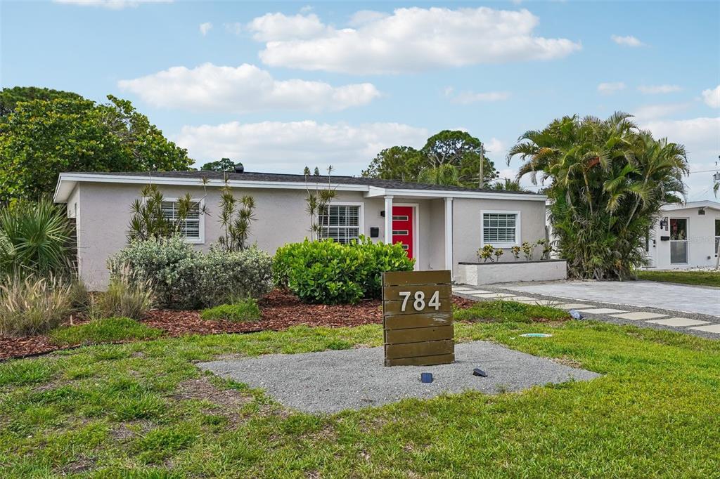 A single-story house with a red front door and a wooden address sign in front — 784 87TH AVENUE N, ST PETERSBURG, FL