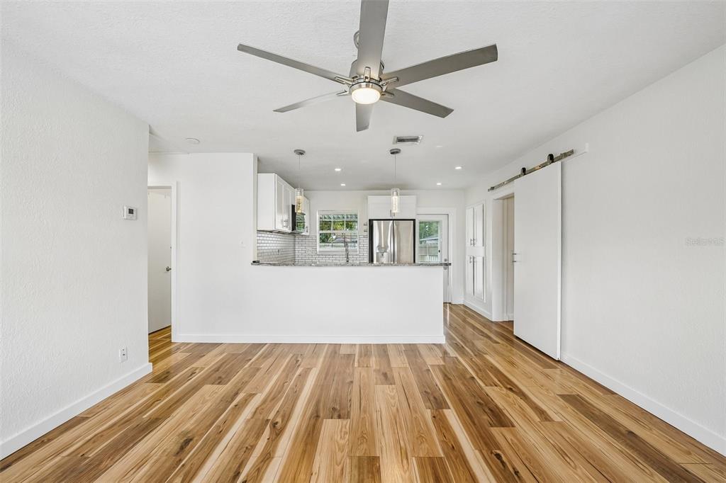 A kitchen with white cabinets and stainless steel appliances overlooks a room with wood flooring — 784 87TH AVENUE N, ST PETERSBURG, FL