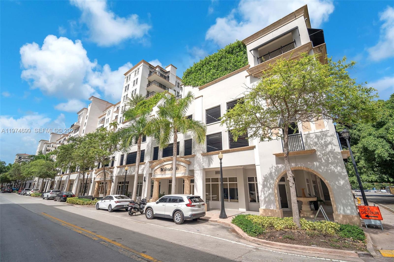 A low-angle exterior view of a multi-story white building with palm trees and parked cars — 4100 Salzedo St # 519, Coral Gables FL 33146, CORAL GABLES, FL